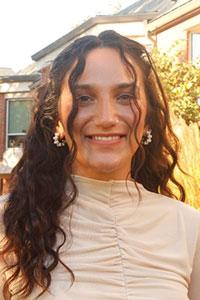 woman with dark brown wavy hair wearing a cream color shirt