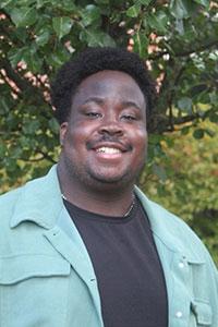 man with brown skin black hair wearing a black shirt and mint jacket